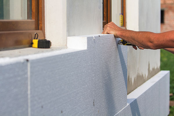 A worker’s hand placing a block of polyurethane foam insulation against a building’s wall.
