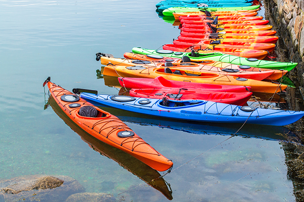 A long row of kayaks moored against a rock wall