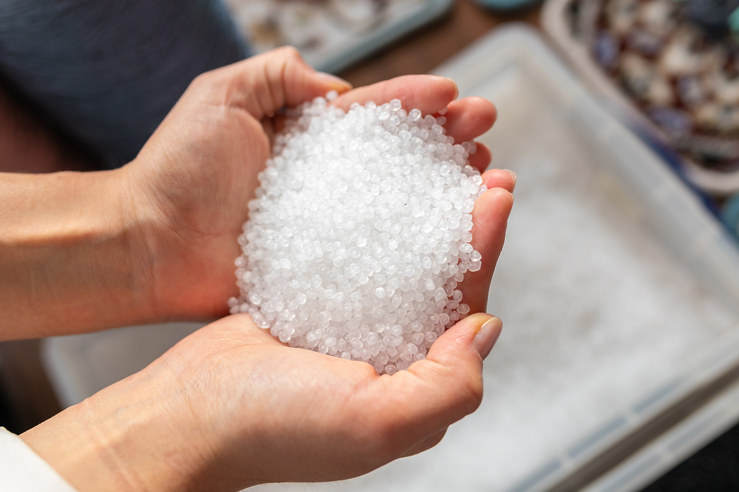 Hands holding a small pile of transparent plastic granules for use in extrusion or thermoplastic molding