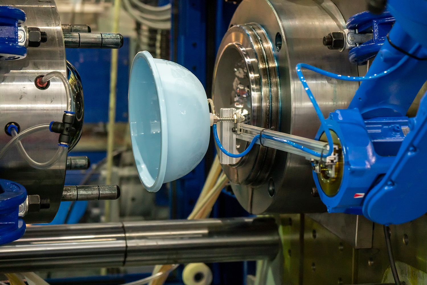 A robotic arm carrying a blue plastic bowl away from the injection molding machine.