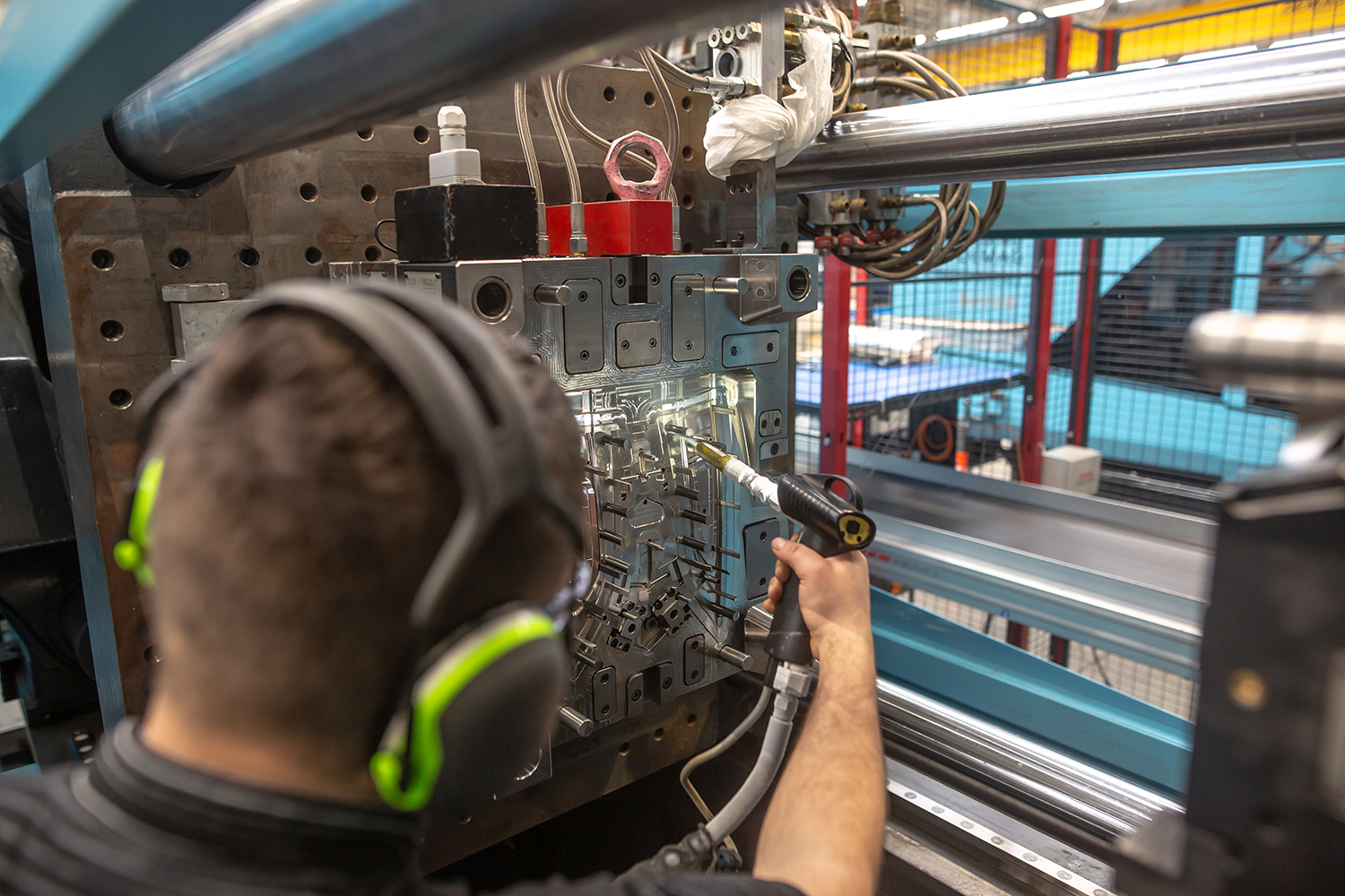 A molding technician performs maintenance on an injection molding machine