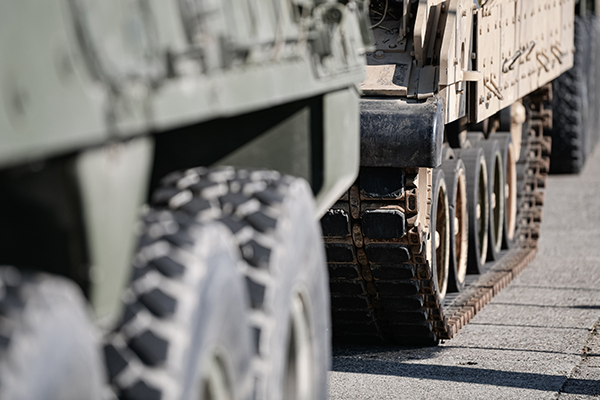 A view of a military tank focusing on the treads, with a transport vehicle and tires out of focus nearer the viewer