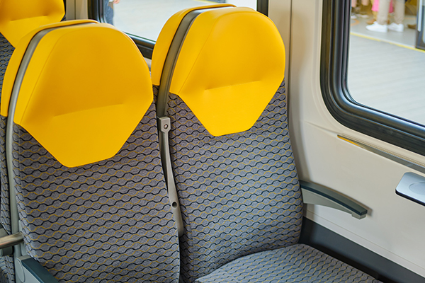 A pair of train seats with bright yellow head-rests and gray seat fabric with a black and yellow wavy pattern