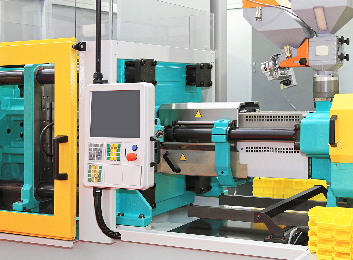 A close view of a plastic injection molding machine, with bright yellow, white, and cyan parts of the frame visible