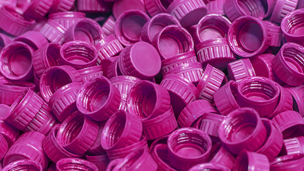 A pile of magenta bottle lids created from thermoplastic materials