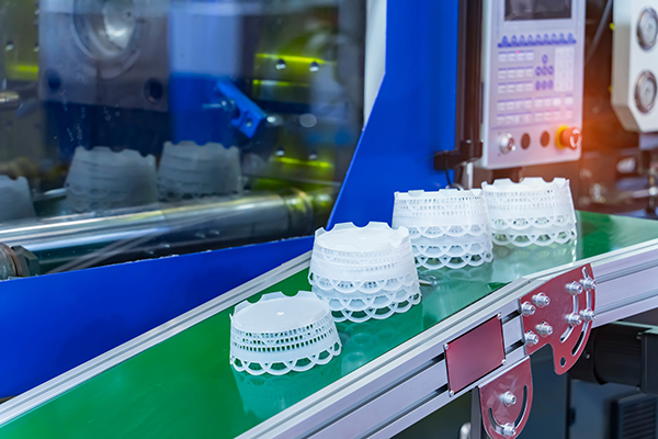 A number of polystyrene containers on a conveyor leading out of an injection molding machine.