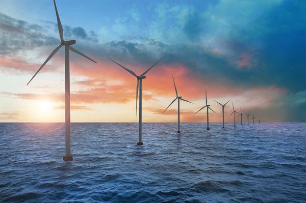 Floating wind turbines installed at sea with the sun setting in the background.