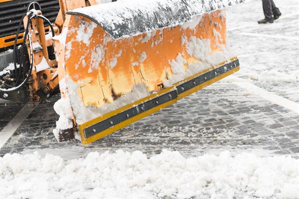poly-lub An orange snowplow pushes snow to the side on a brick road.