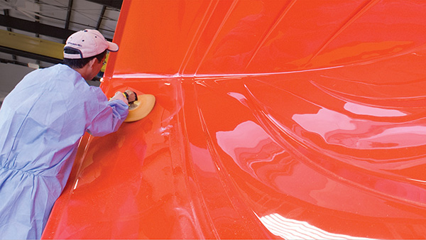 A worker polishes a red boat hull mold.