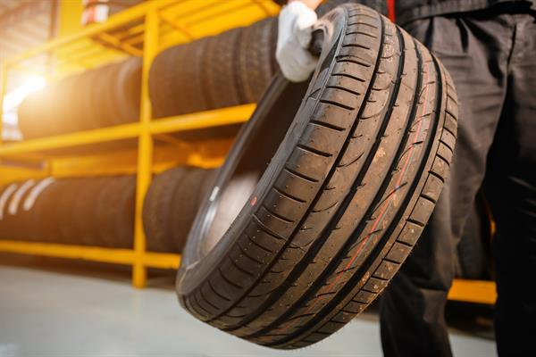 A person holds a tire with a gloved hand at a tire repair shop.